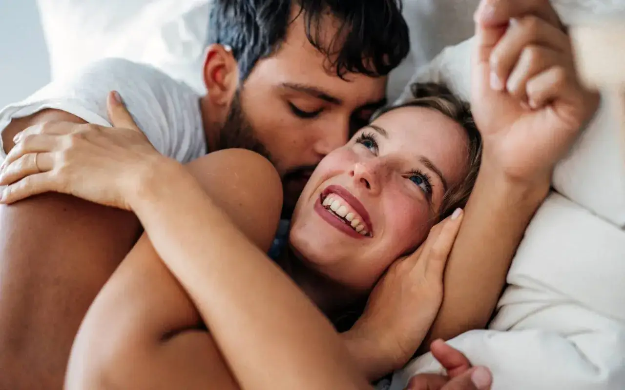 Ein Mann umarmt eine Frau im Bett. Sie l&auml;chelt ihn an. Manchmal hat man keine Lust auf Sex in der Schwangerschaft, aber N&auml;he ist trotzdem sch&ouml;n.