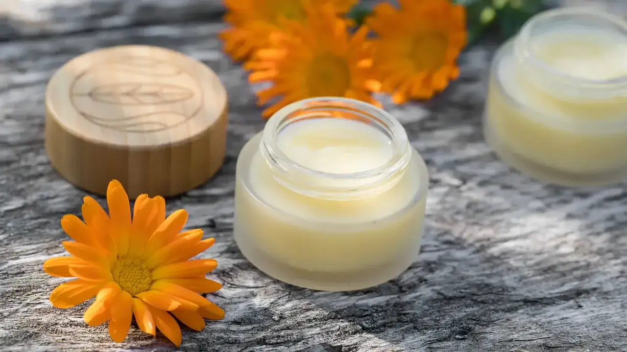 Ringelblumencreme in Gl&auml;schen, umgeben von leuchtenden Ringelblumen. Die Ringelblume ist bekannt f&uuml;r ihre Heilwirkung.