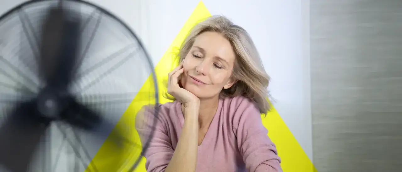 Frau genie&szlig;t k&uuml;hle Brise vom Ventilator. Hitzewallungen ohne Wechseljahre? Abk&uuml;hlung tut gut.