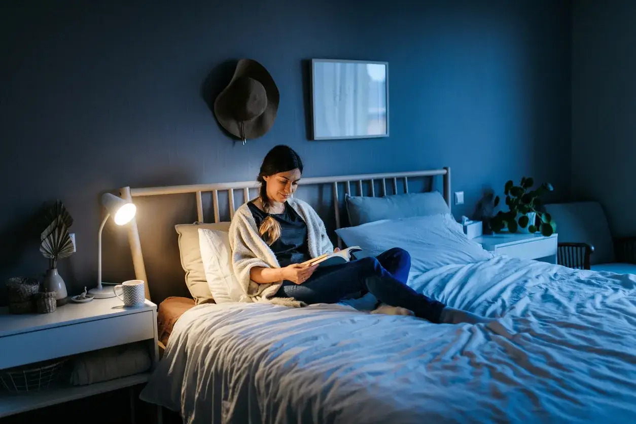 Frau liest im Bett, um Stress zu reduzieren. Gem&uuml;tliche Atmosph&auml;re mit Nachttischlampe und Buch.