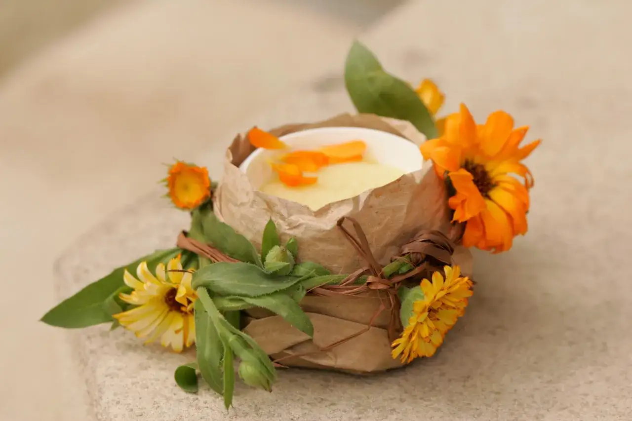 Selbstgemachte Ringelblumensalbe in einem Becher, verziert mit frischen Ringelblumen und Bl&auml;ttern.
