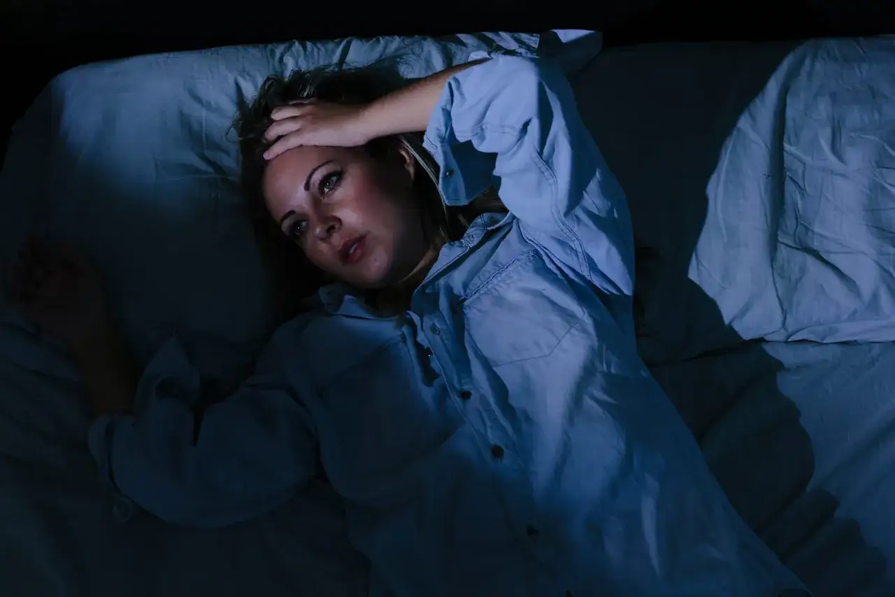 Frau liegt im Bett, h&auml;lt sich die Stirn. Ihre Augen sind weit ge&ouml;ffnet, sie wirkt besorgt. Ein Bild von stress symptome frau.