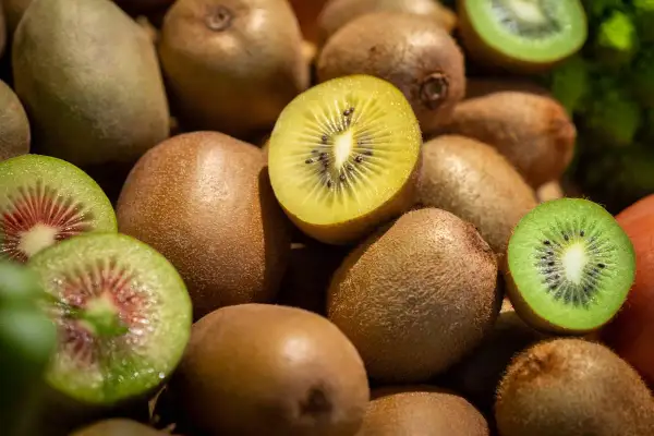 Ein Haufen Kiwis, einige ganz, andere aufgeschnitten, zeigen ihr grünes und gelbes Fruchtfleisch. Diese Früchte sind eine natürliche Quelle für Melatonin.